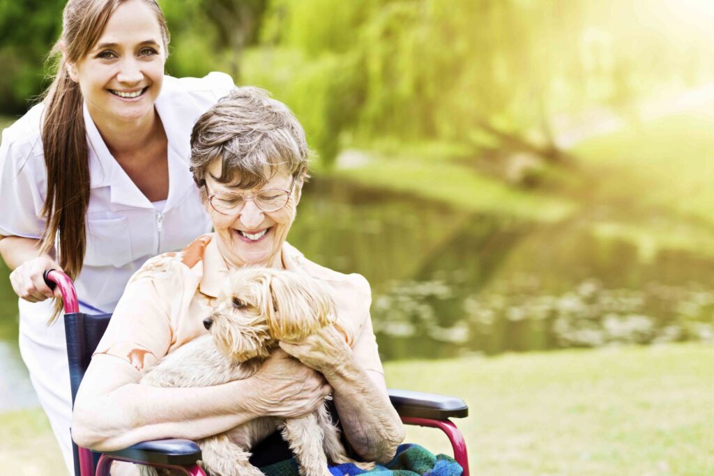 senior lady holding her dog while smiling with a healthcare worker