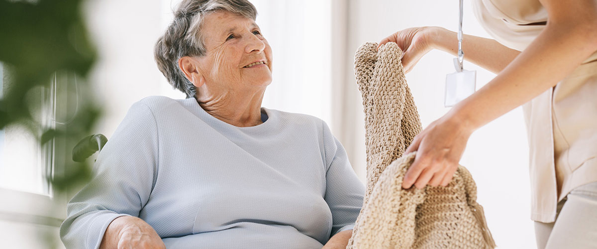 A senior living staff member brings a blanket to a senior in memory care