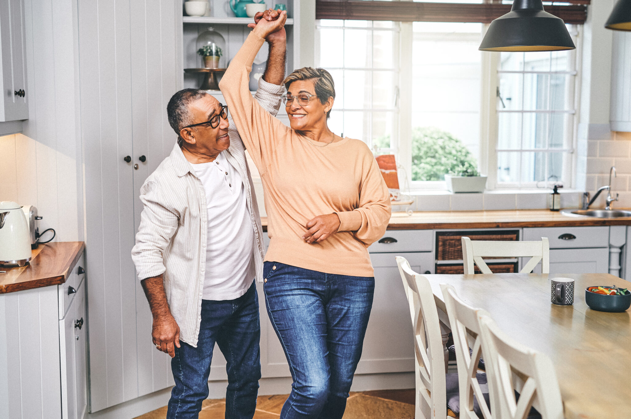 A senior couple twirl and dance in their kitchen
