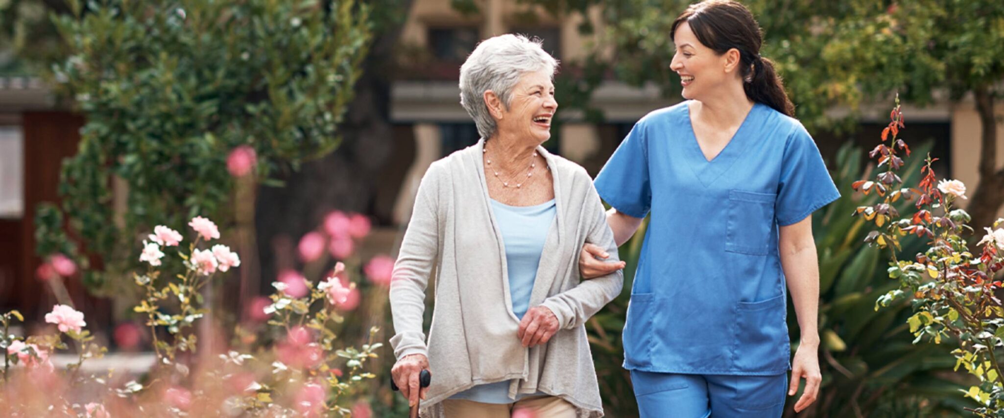 A senior woman gets assistance walking through a flower garden