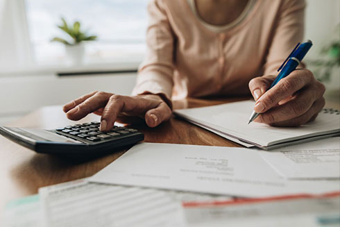 Close up on a senior woman's hands while calculating taxes with a calculator.