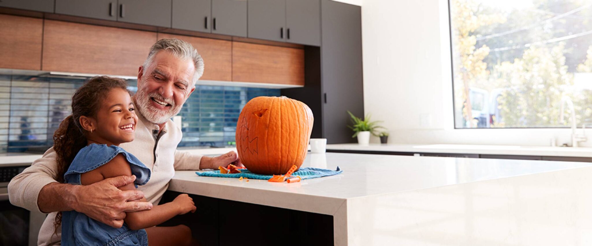 senior man helps his granddaughter carve a pumpkin