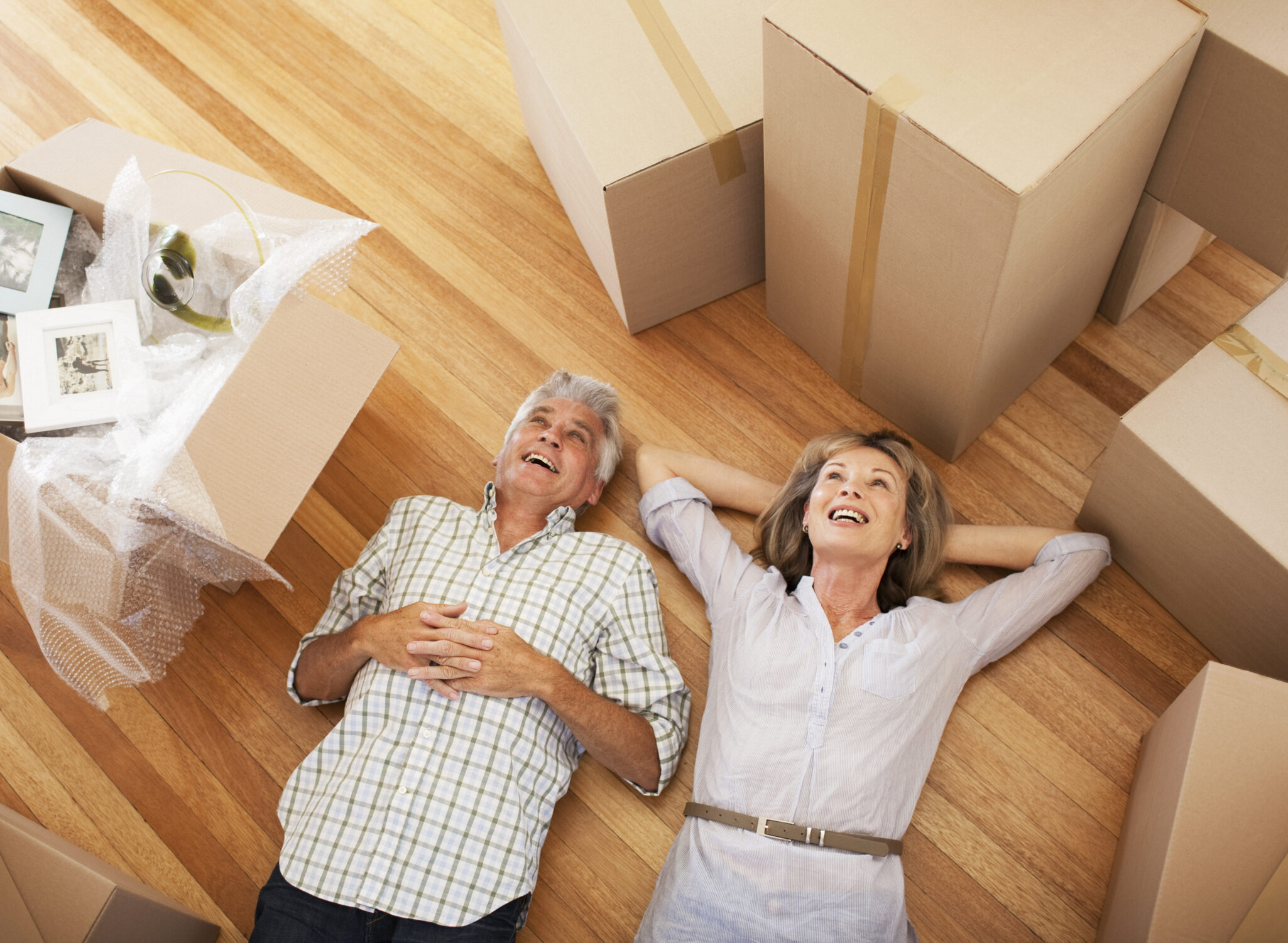 A senior couple lay on the floor, surrounded by moving boxes, daydreaming about their new place