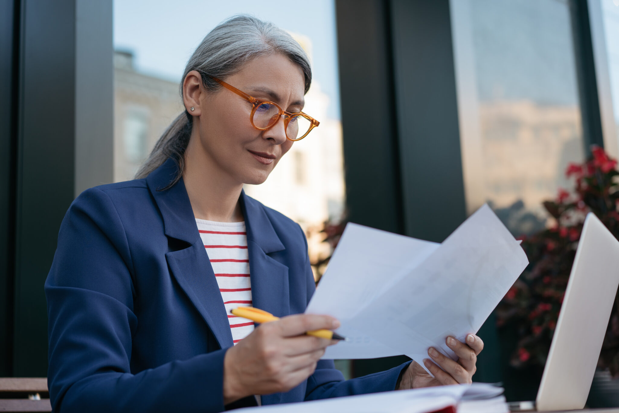 An older woman sights outside in on a balcony in a city and looks at paperwork