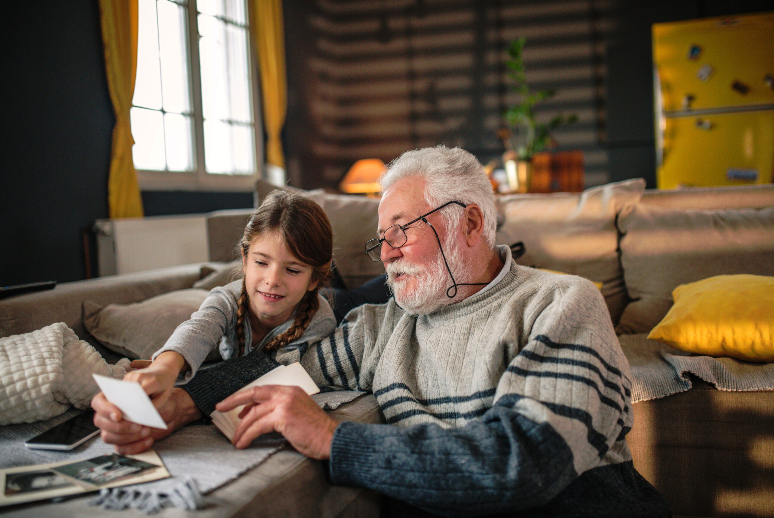 Grandfather and granddaughter looking at photos on the couch together