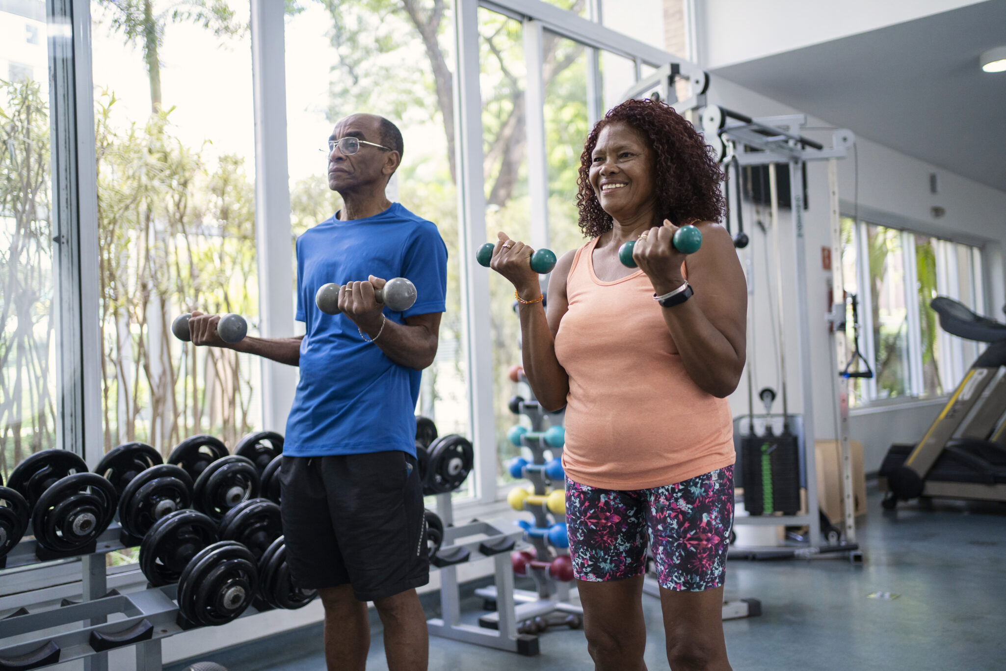 An older man and older woman lift hand weights in the gym