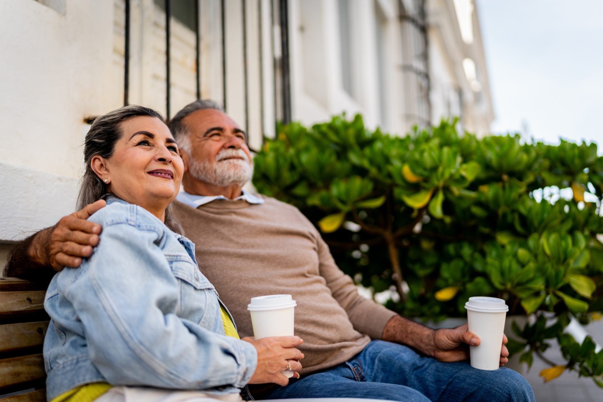Senior couple sitting on bench holding coffee