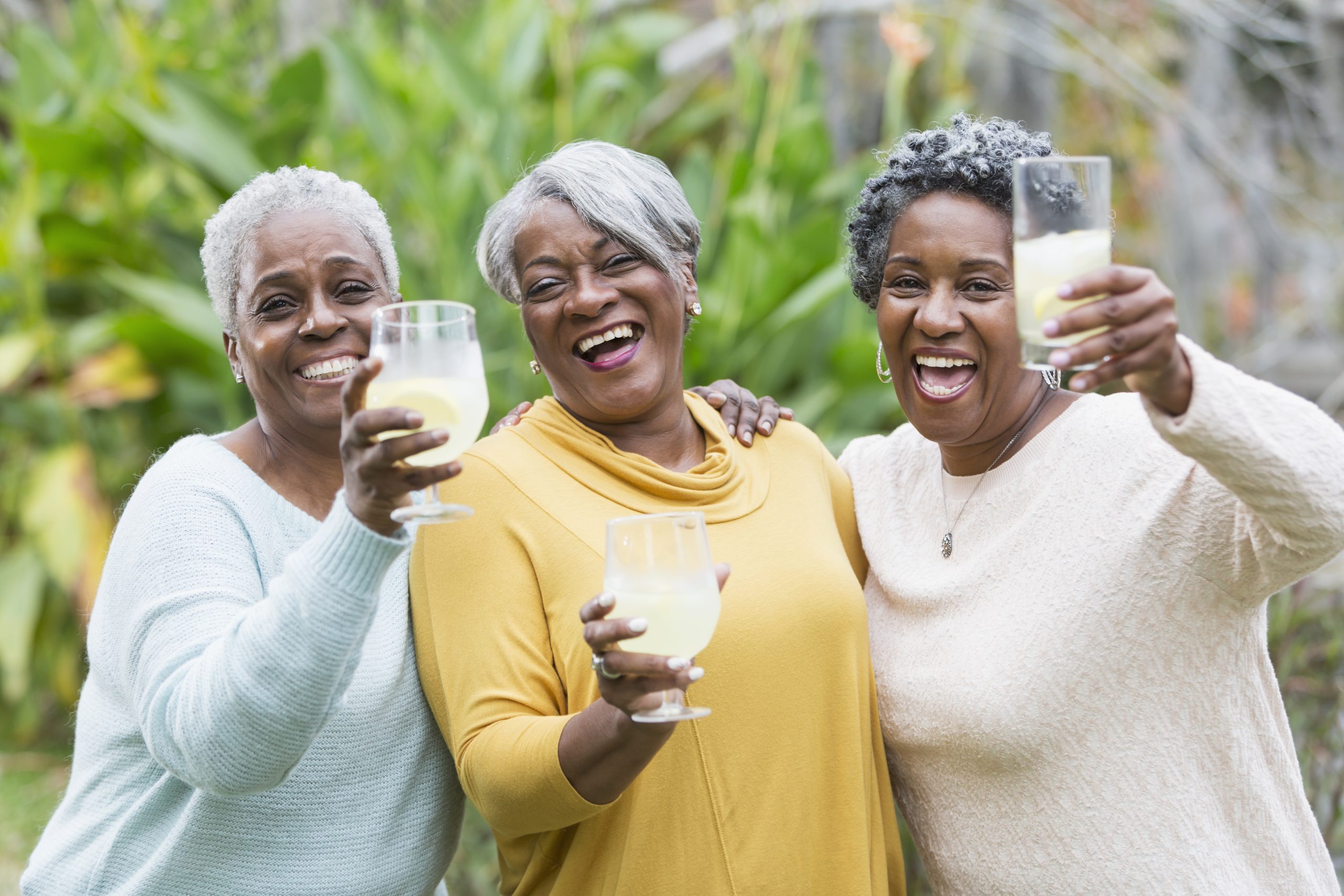 Three happy senior women outdoors holding up glasses of lemonade